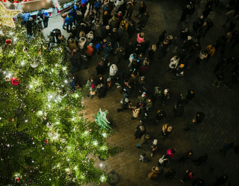Vista dall’alto di una piazza illuminata per Natale con albero, bancarella e persone che passeggiano di sera