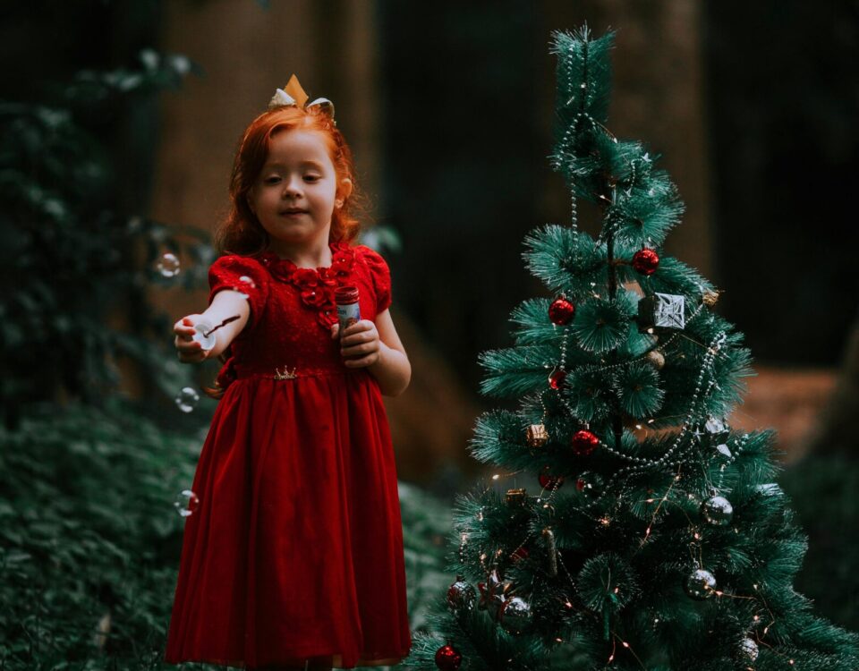 bambina in un bosco che coglie un fiore accanto a un albero di Natale, atmosfera fiabesca invernale